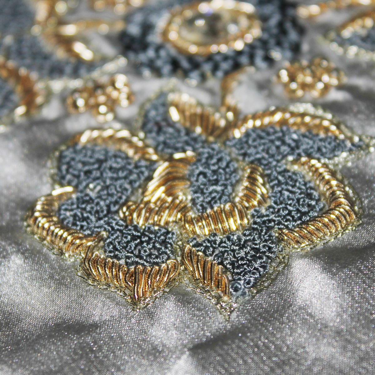Zardozi Embroidery | The India Detailed zardozi embroidery shows dark gray and gold thread on shimmering silver fabric, a beautiful example of Indian.
